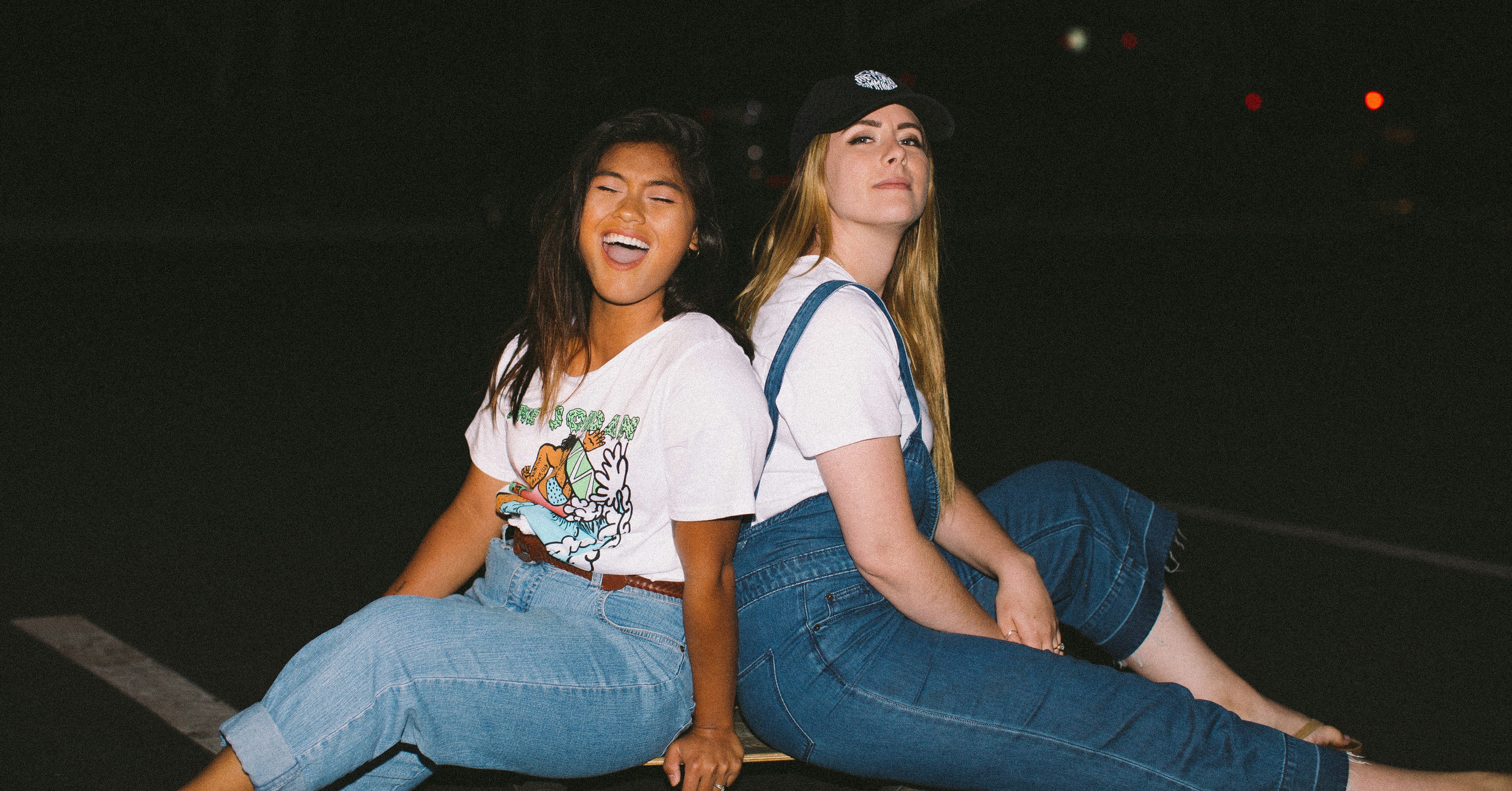 Two young people sitting back to back. One is laughing and the other is smiling.